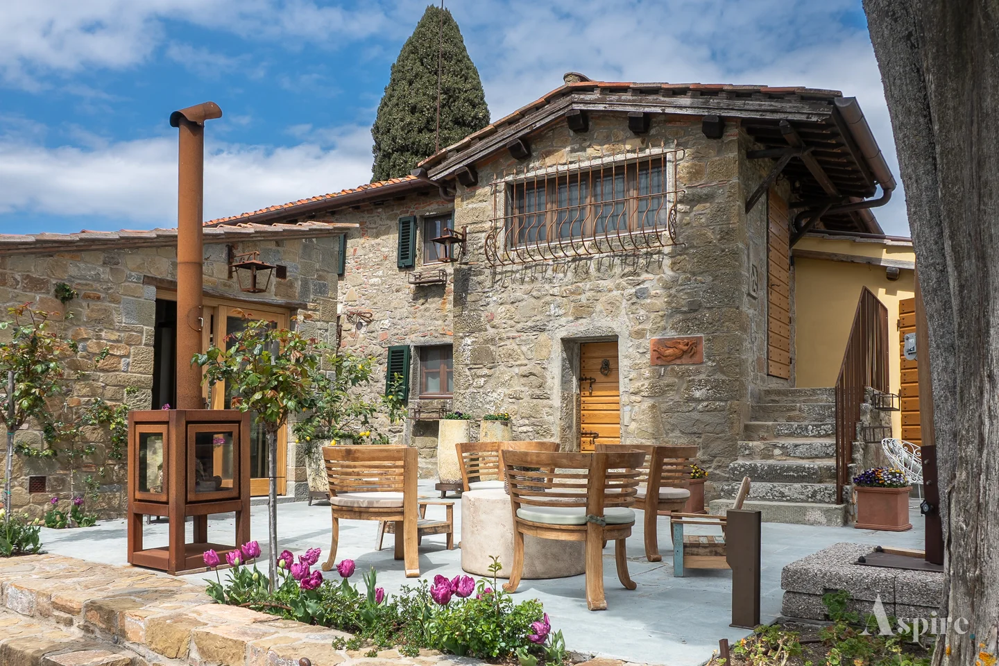 Stone villa terrace set for dining beneath a cypress tree
