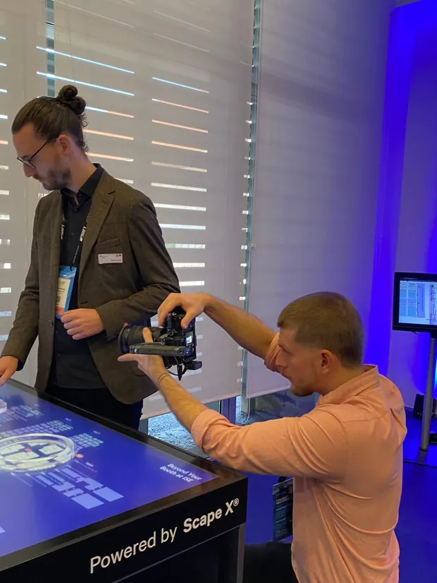 Two people filming a product demonstration on a phone at an exhibition stand